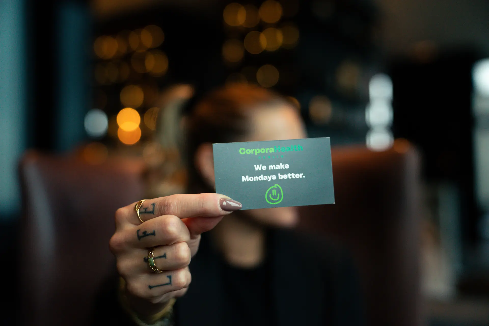 Hand hält eine dunkle Visitenkarte von CorporaHealth mit dem Claim We make Mondays better